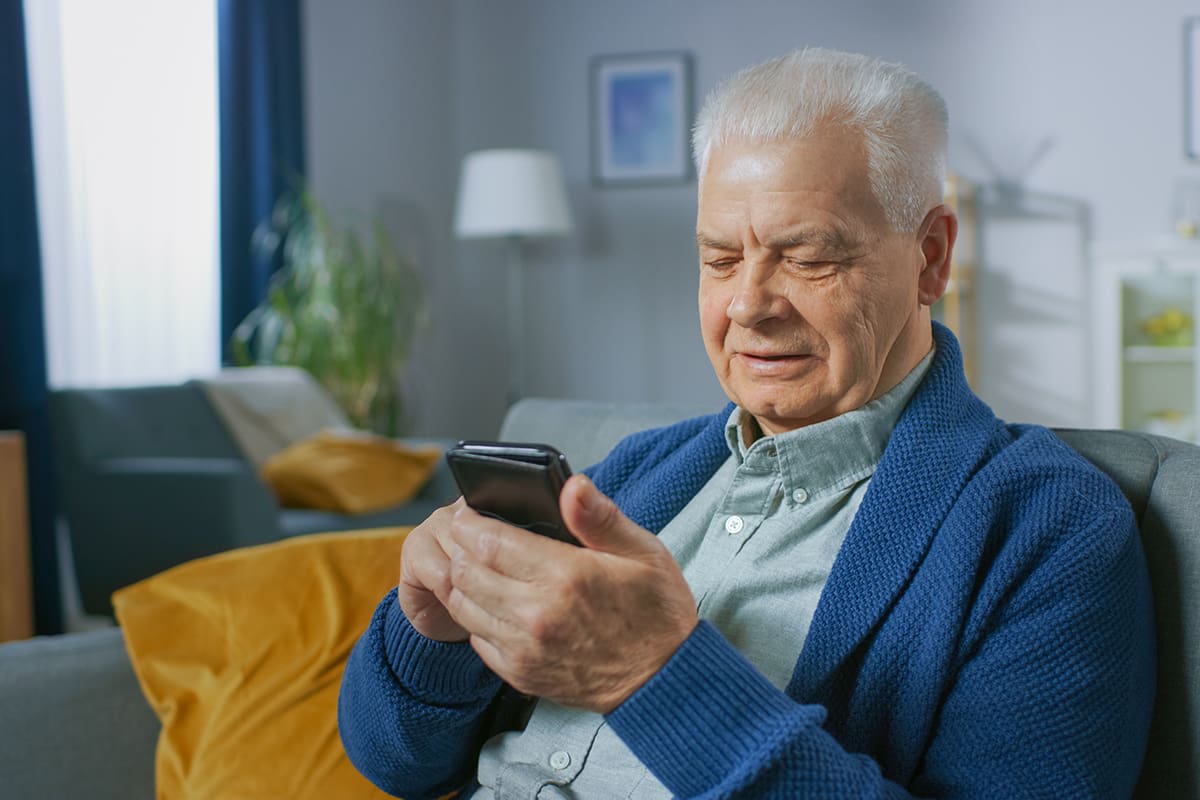 Portrait of Progressive Senior Man Sitting in His Living Room Easily Uses Smartphone, Does Touching Gestures and Feels Very Comfortable with New Technologies.