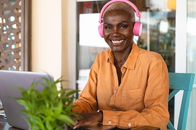 Smiling African American woman using laptop and listening music with headphones