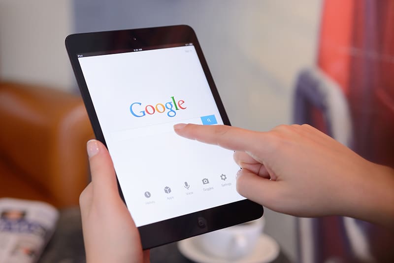 Womans hands holding a iPad Mini displaying Google Application in a coffee shop.