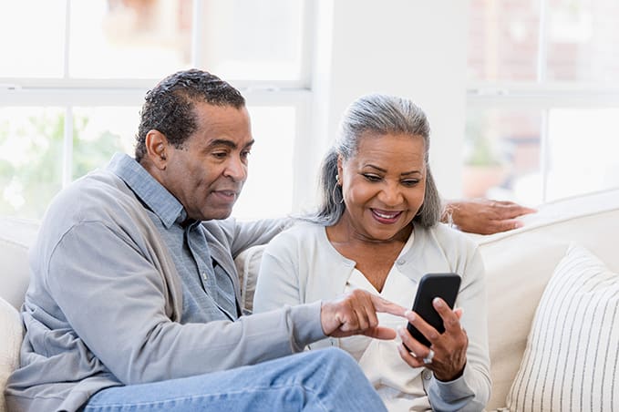 Husband and wife sit on the couch and read an article on the phone.