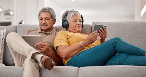 Senior Couple on a sofa using and listening to mobile devices.