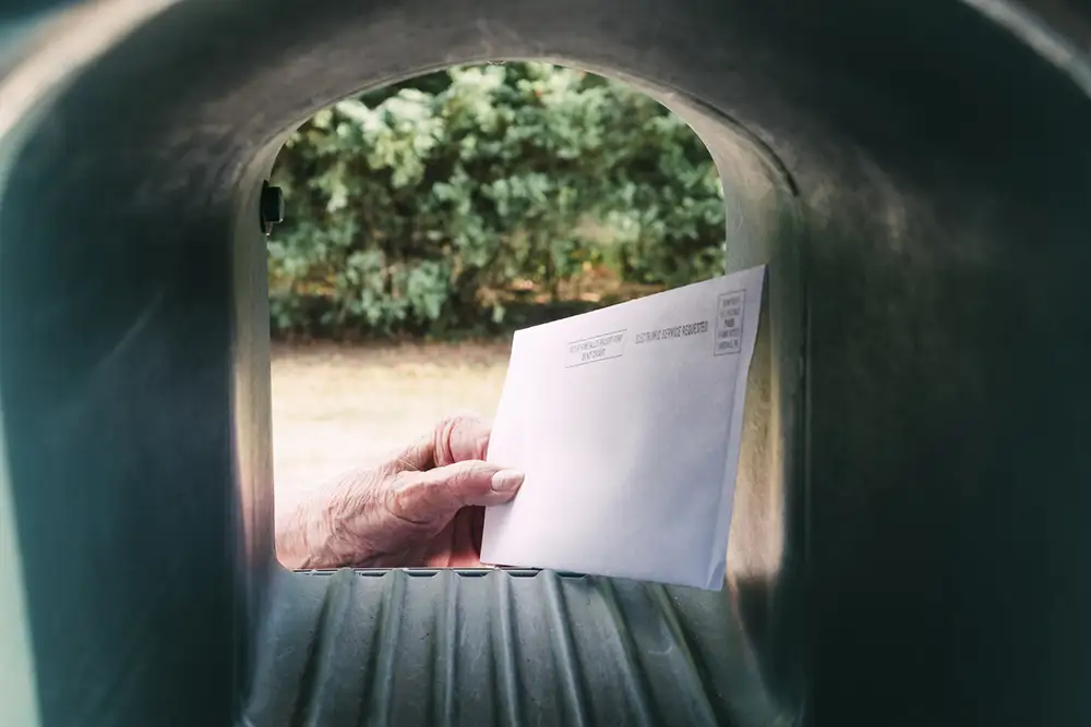 An elderly hand is getting a mail in ballot form out of the mailbox.