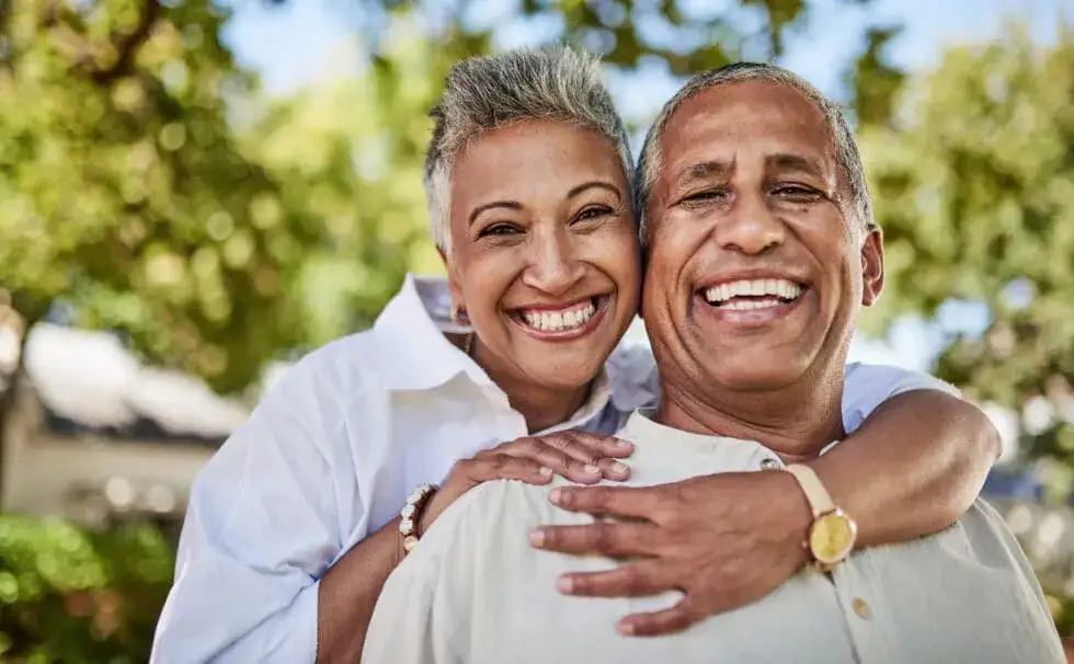 Happy elderly couple in a garden, hug, relax and bonding in their senior living community