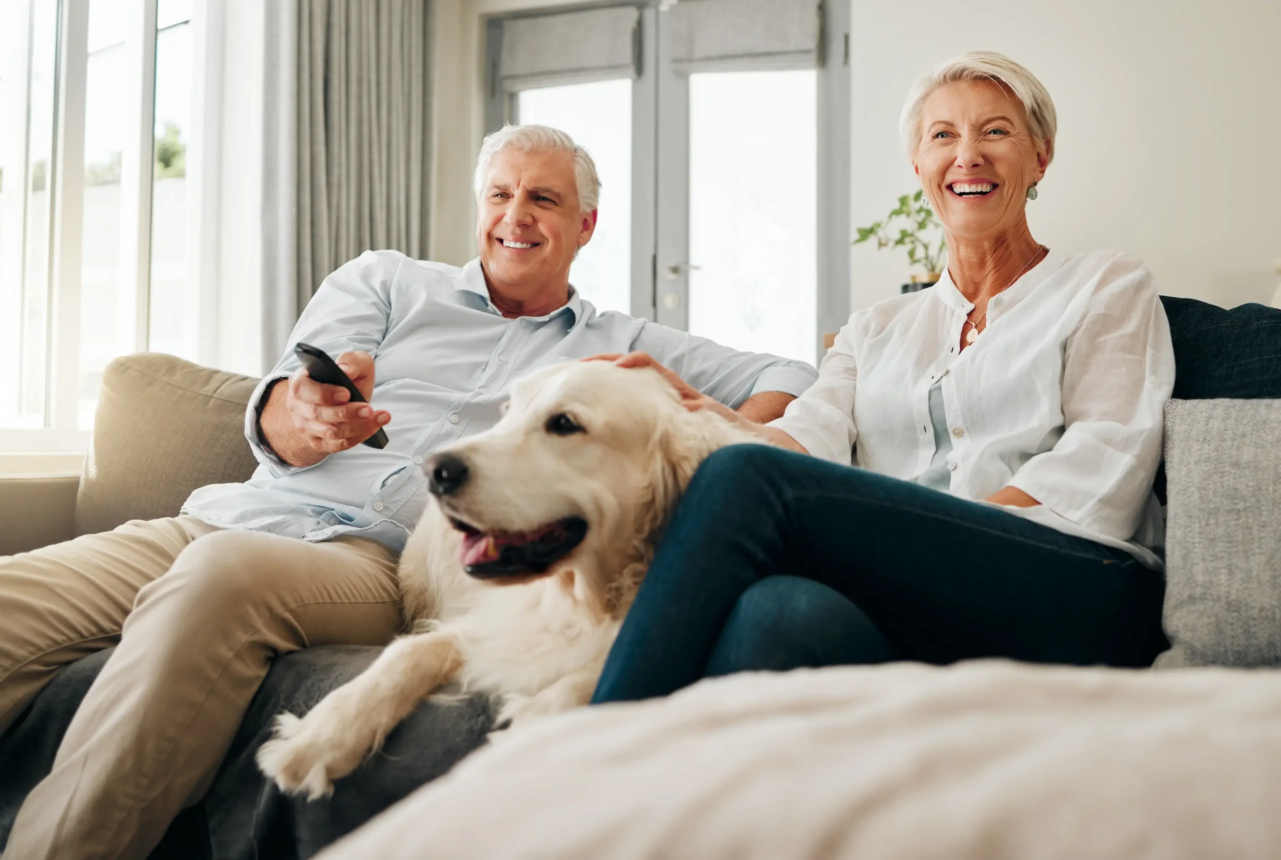 iStock-1777667498 Senior cople watching TV from their couch with their Golden Retriever